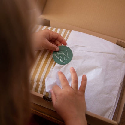 Person holding a green sticker with a logo over white fabric in a cardboard box.