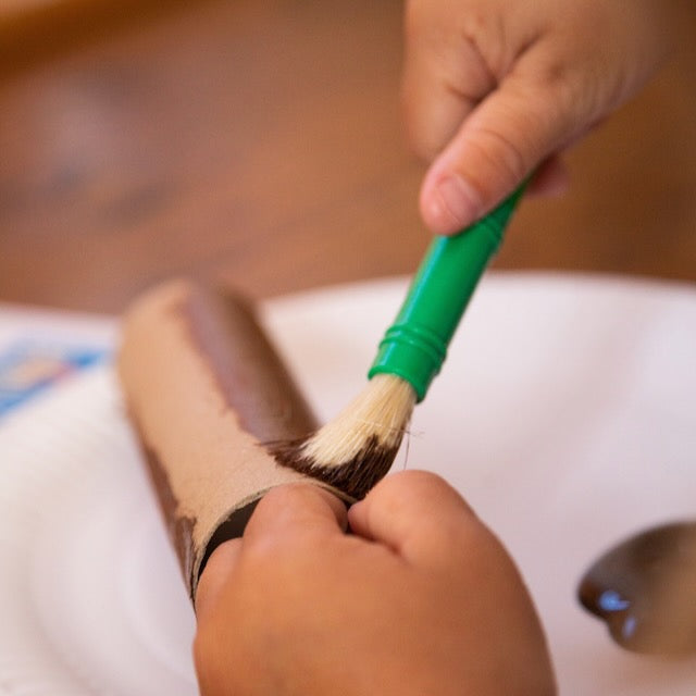 Person cleaning a dog's paw with a green brush on a white surface.