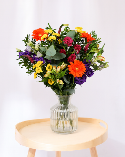 Colorful bouquet of flowers in a clear vase on a wooden table with a white background