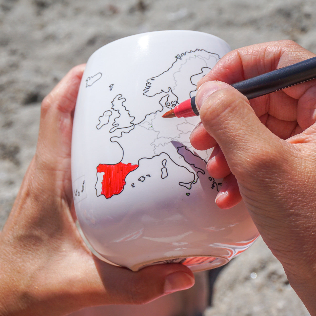 Person coloring a map of Europe on a ceramic mug with a red marker.