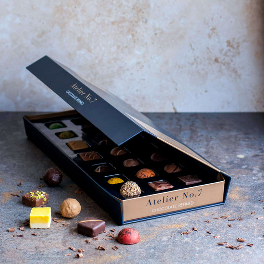 Open box of chocolates from Atelier No. 7 on a textured surface with a neutral background