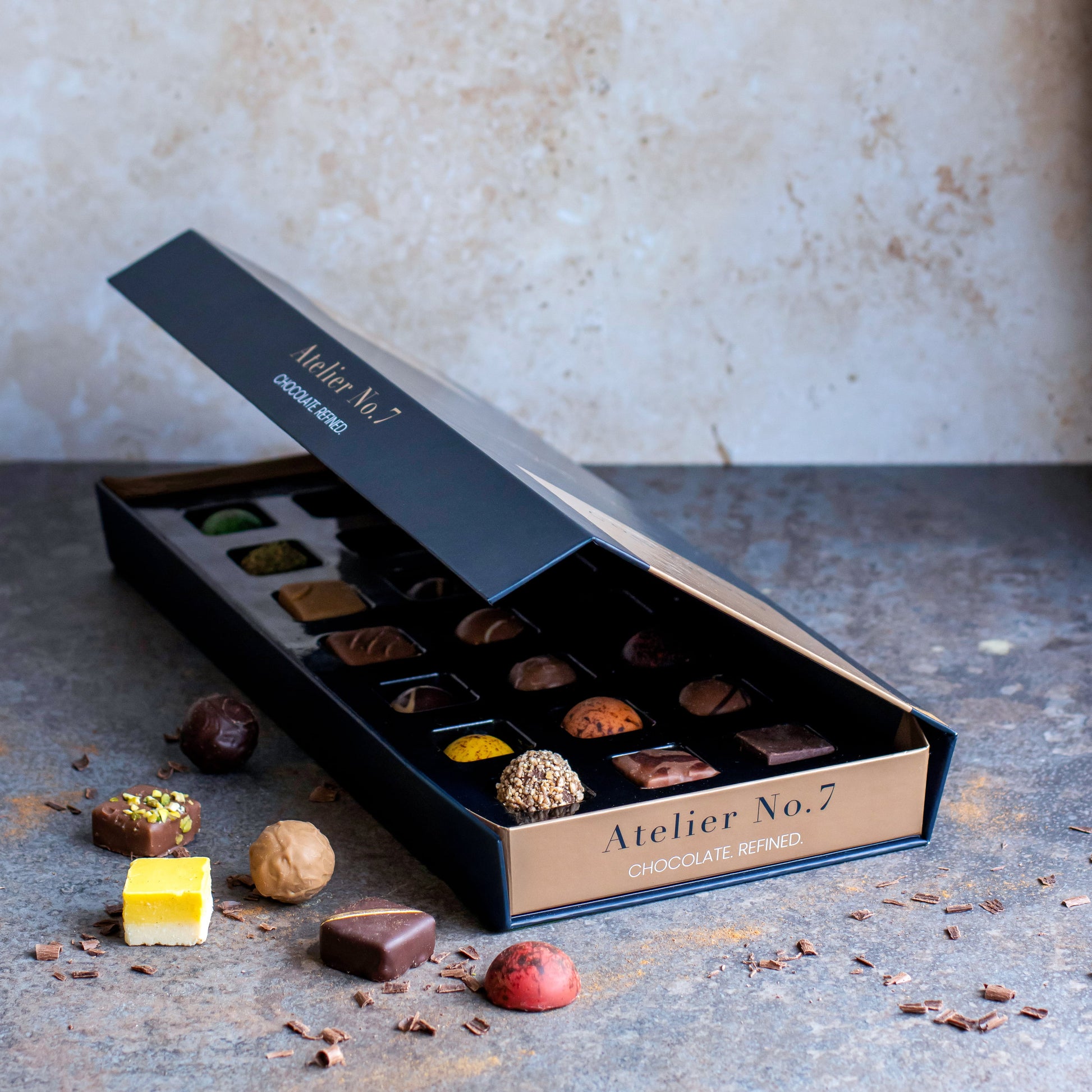 Open box of chocolates from Atelier No. 7 on a textured surface with a neutral background