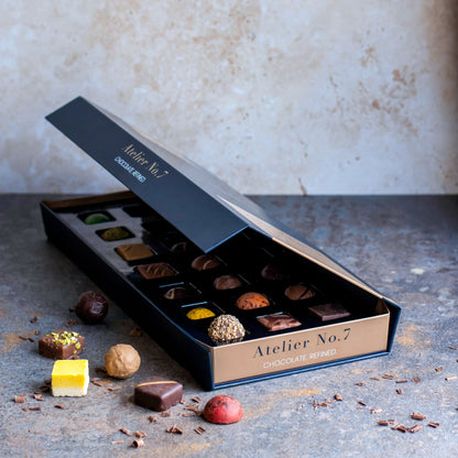 Open box of chocolates from Atelier No. 7 on a textured surface with a neutral background