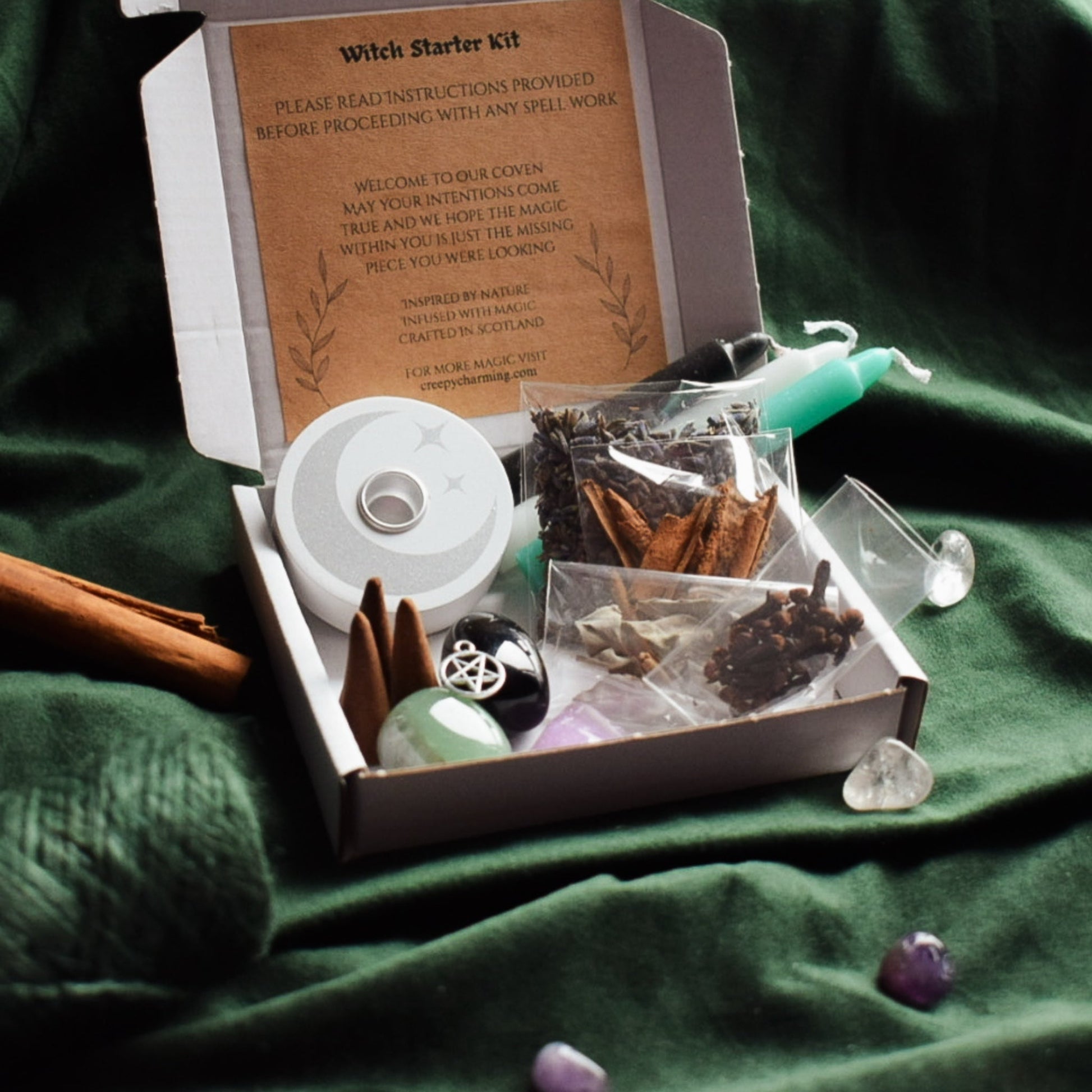 Witch starter kit with spellbook, candle, and crystals on a green fabric background