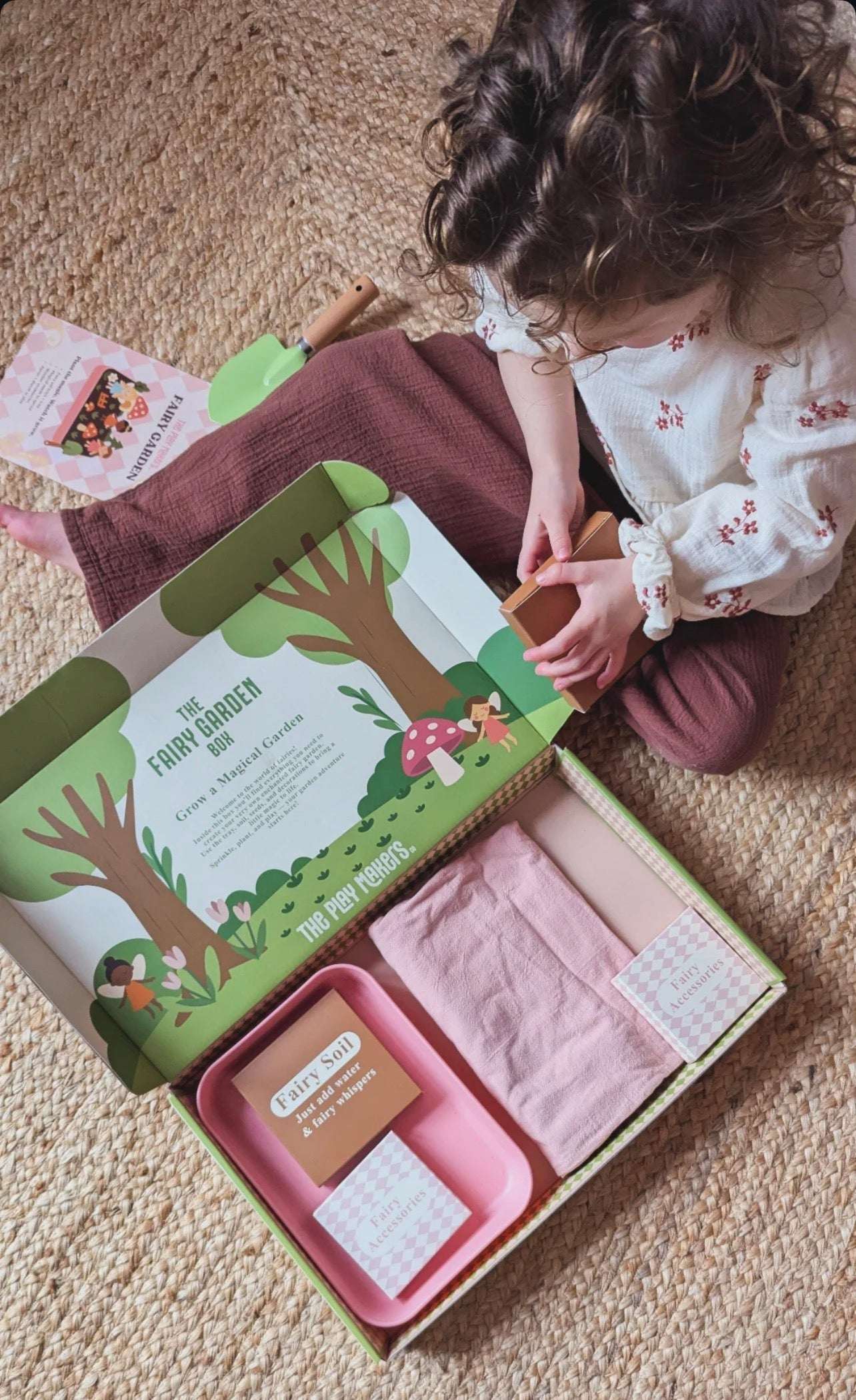 Child opening a baby gift box with pink items and a green tree design on the lid.