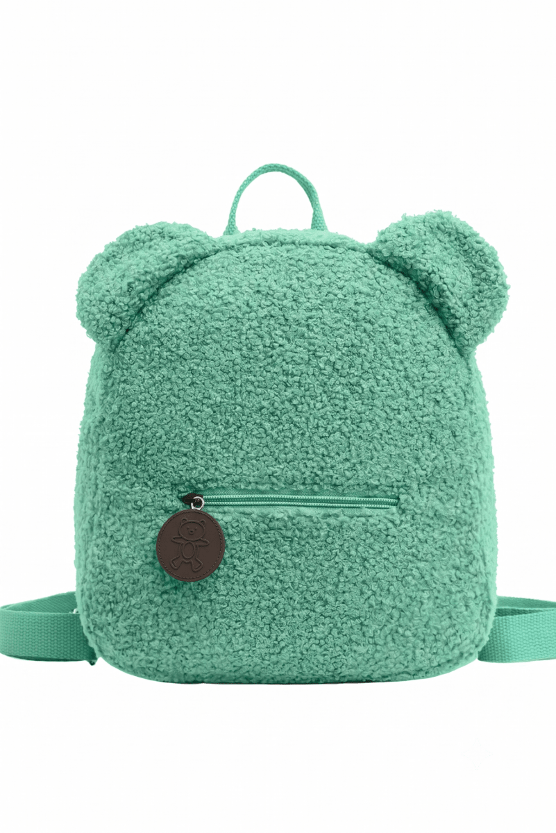 A mint green teddy fleece backpack with bear ears on top, a front zip pocket, and a round brown leather logo charm, shown against a plain white background.