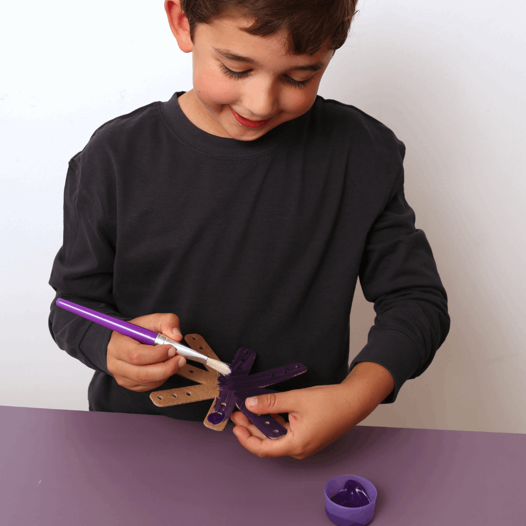 Child painting a purple object with a brush on a white background
