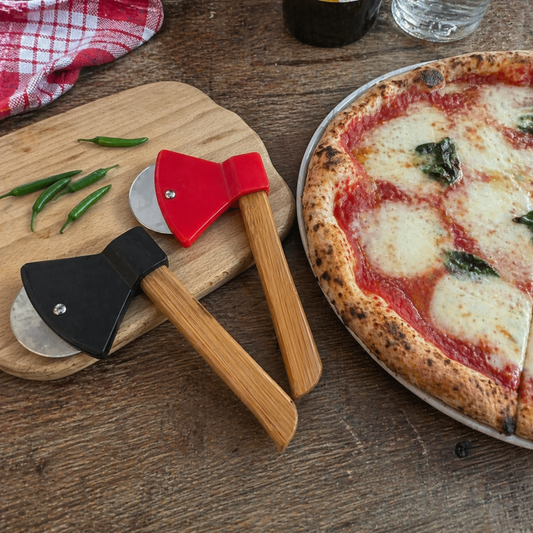 Wooden pizza cutter with red and black ends next to a pizza on a wooden table.