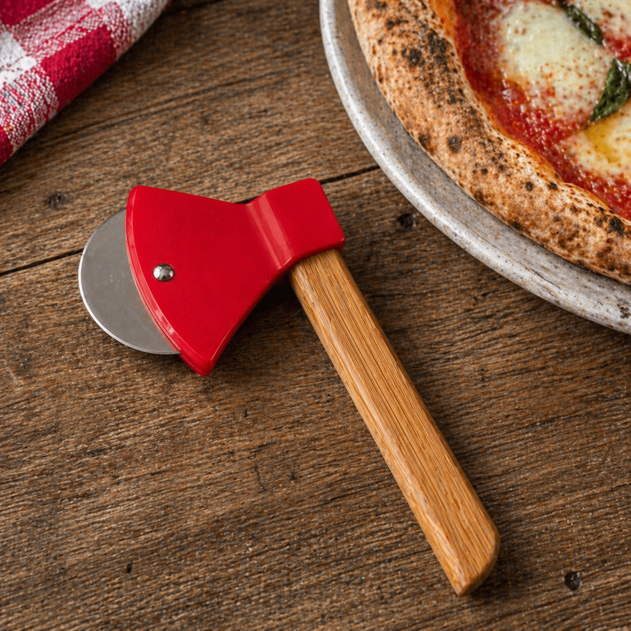 Red pizza cutter with wooden handle on a wooden table next to a pizza