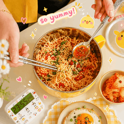 Hot bowl of noodles with a spoon and chopsticks, surrounded by various dishes and a timer on a light background.