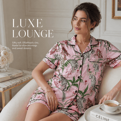 Woman wearing a pink pajama set with zebra print sitting on a couch with a coffee cup.