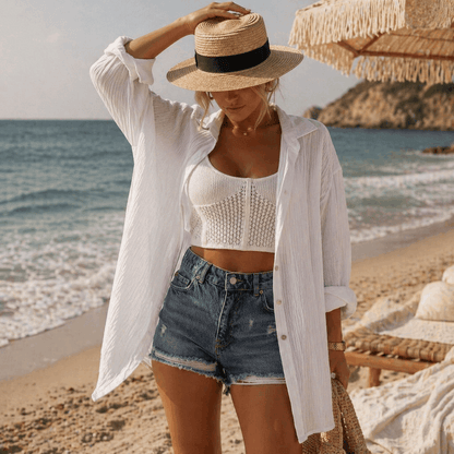 Woman on a beach wearing a white shirt, denim shorts, and a straw hat with a black band.