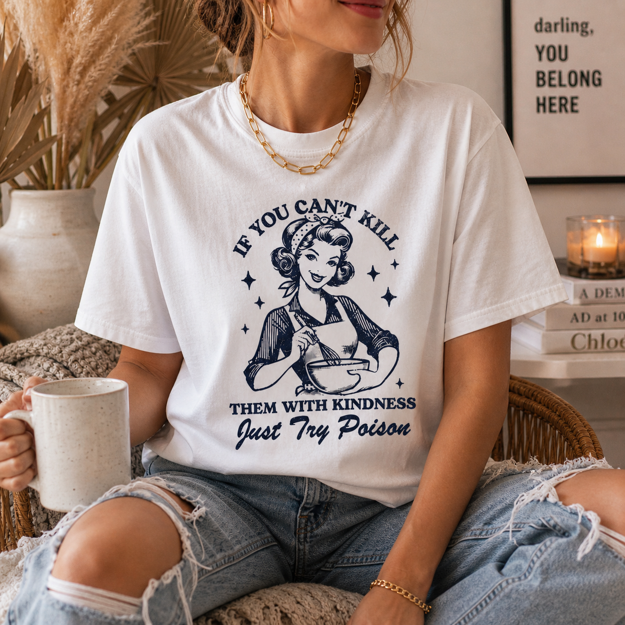 Person wearing a white t-shirt with a graphic and text, holding a mug in a cozy indoor setting.