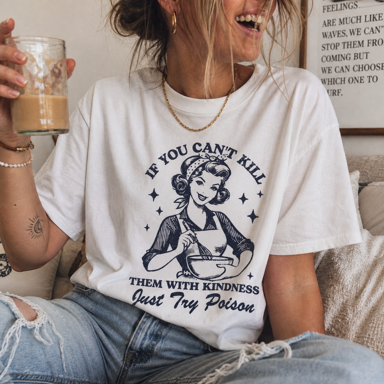 Person wearing a white t-shirt with a graphic and text, holding a glass of coffee.