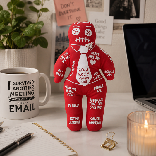 Red plush toy with humorous sayings on a desk with a mug and laptop.