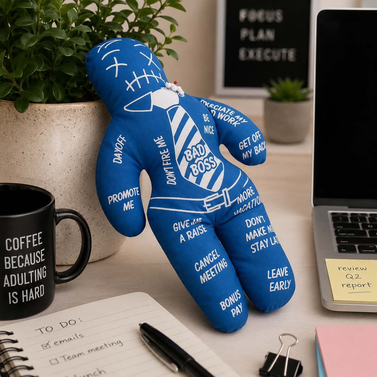 Blue plush toy with humorous sayings on a desk with a laptop and coffee mug.
