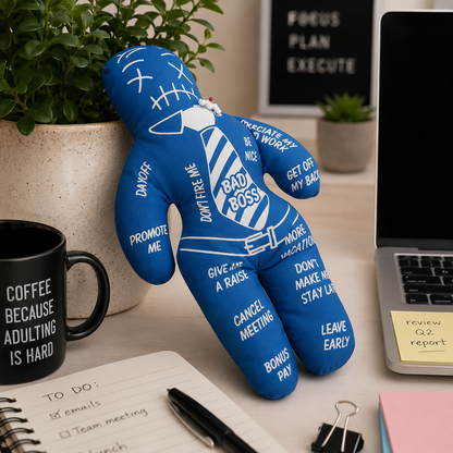 Blue plush toy with humorous sayings on a desk with a laptop and coffee mug.