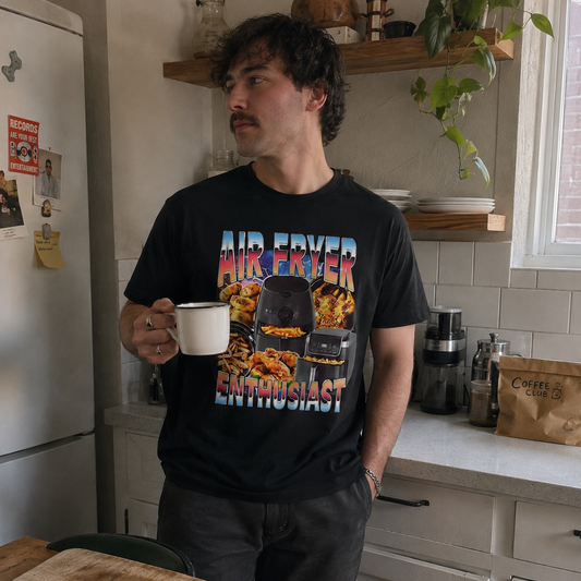 Man in a kitchen holding a mug, wearing a black t-shirt with colorful graphics and text.