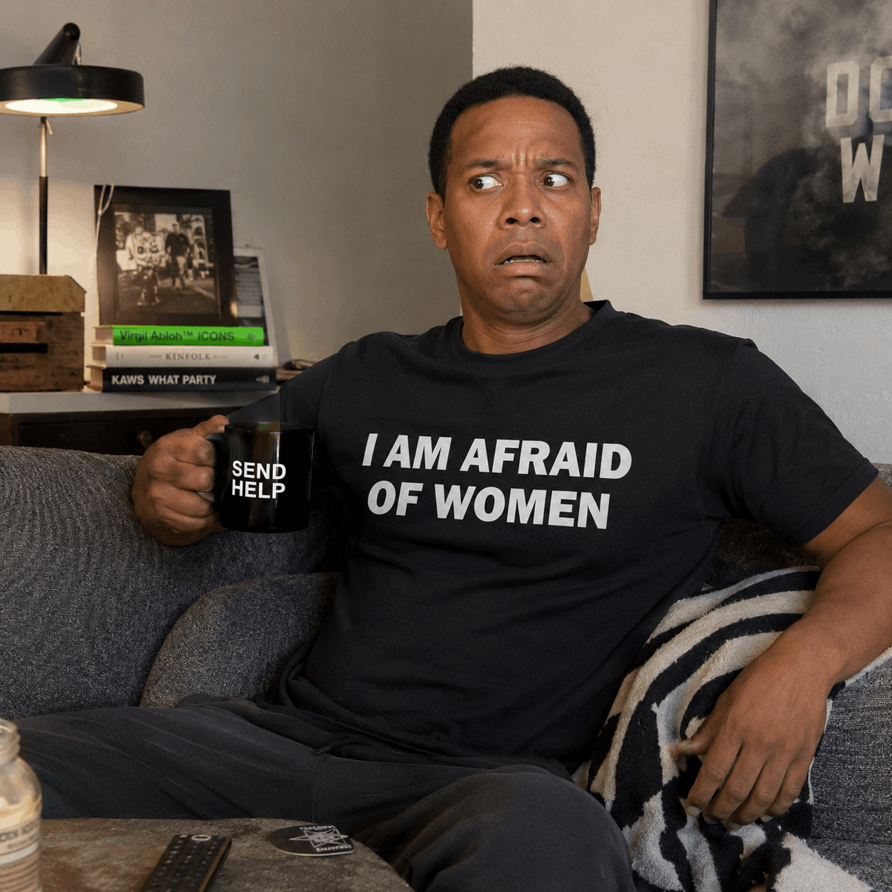 Man sitting on a couch holding a mug with text, wearing a shirt with a humorous message.