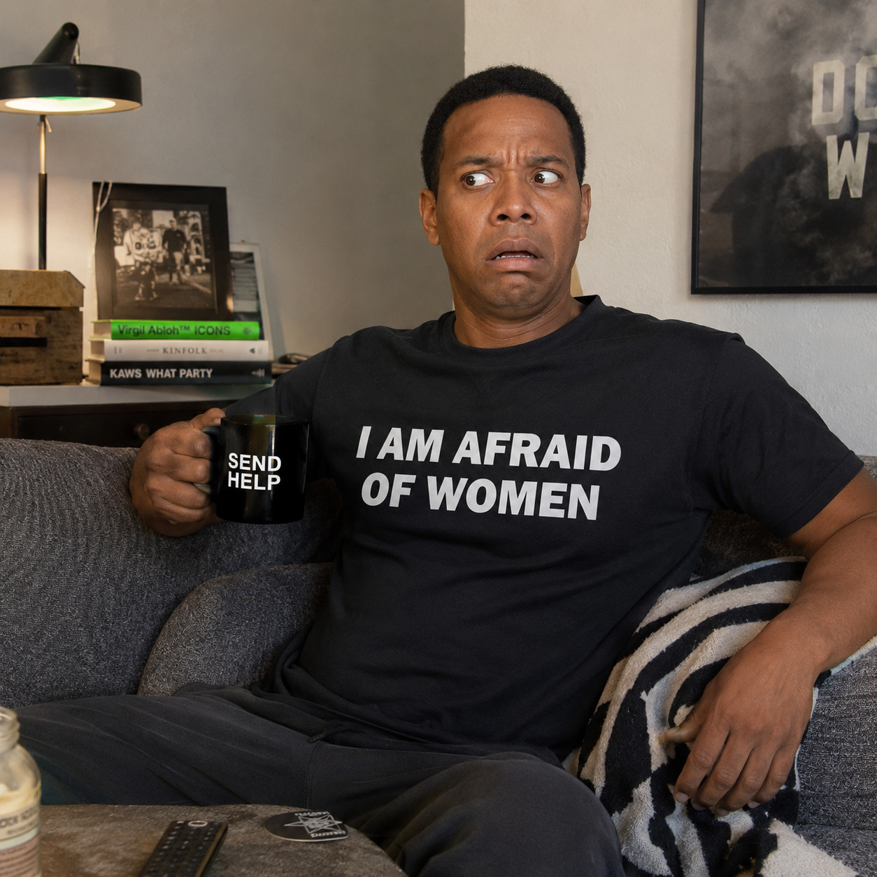Man sitting on a couch holding a mug with text, wearing a shirt with a humorous message.