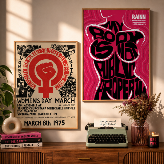 Framed posters on a wall with a typewriter and books on a wooden desk.