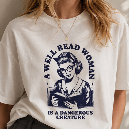 White t-shirt with graphic of a woman reading a book and text 'A well-read woman is a dangerous creature'.