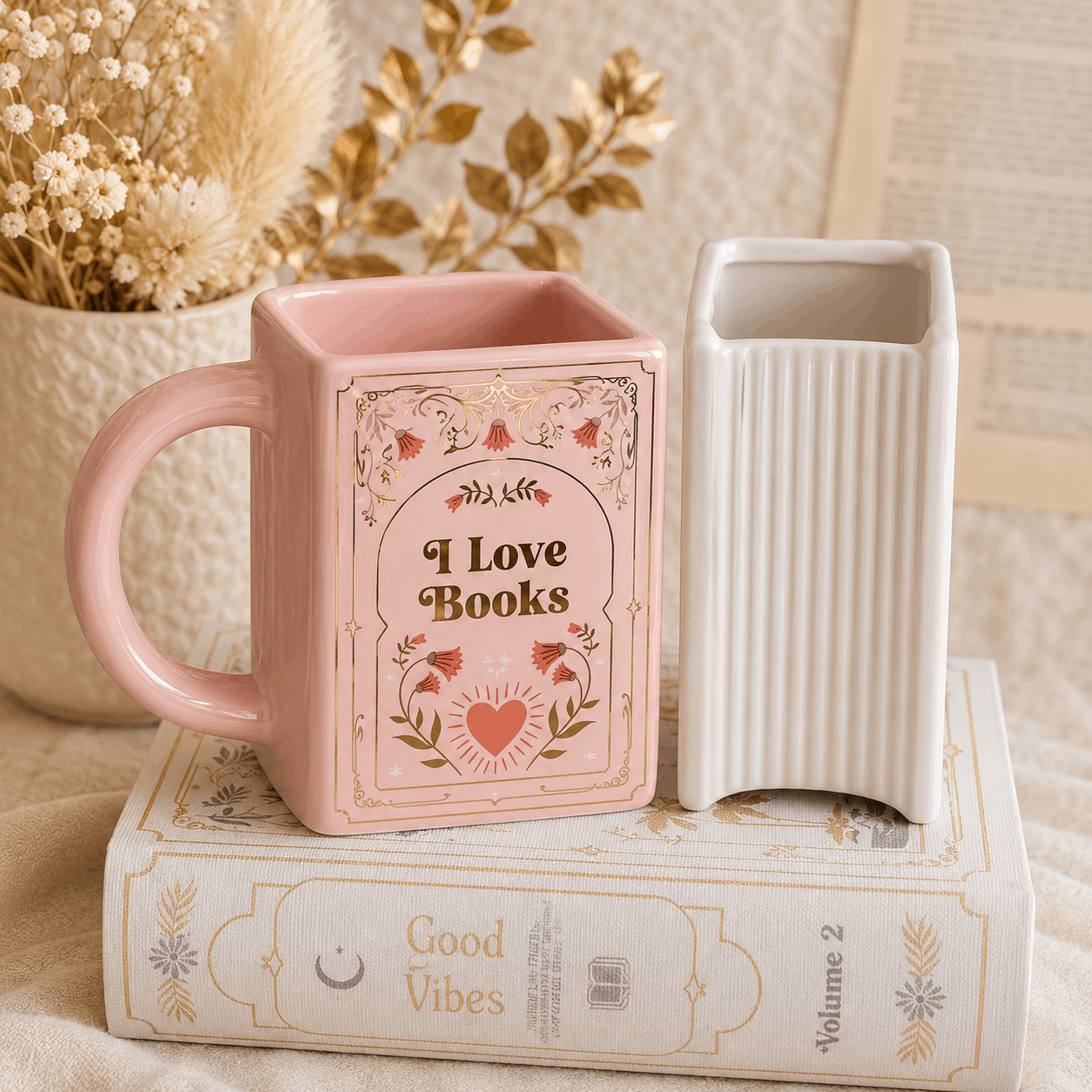 Pink mug with 'I Love Books' design on a stack of books with a white vase next to it.