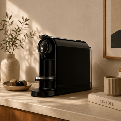 Black coffee machine on a wooden surface with decorative items in a warm-toned room.