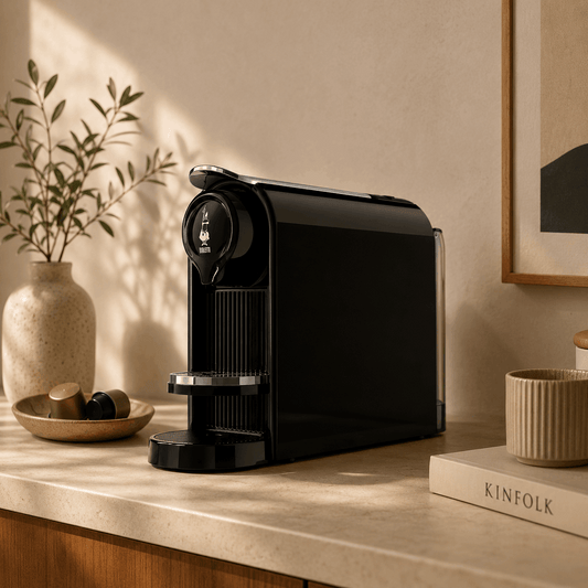 Black coffee machine on a wooden surface with decorative items in a warm-toned room.
