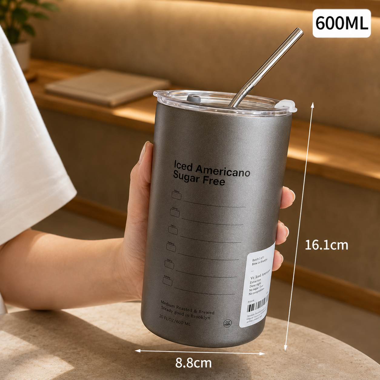 Gray tumbler with measurements and text held by a person indoors