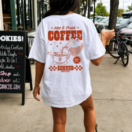 Person wearing a white t-shirt with a coffee-themed design outdoors.