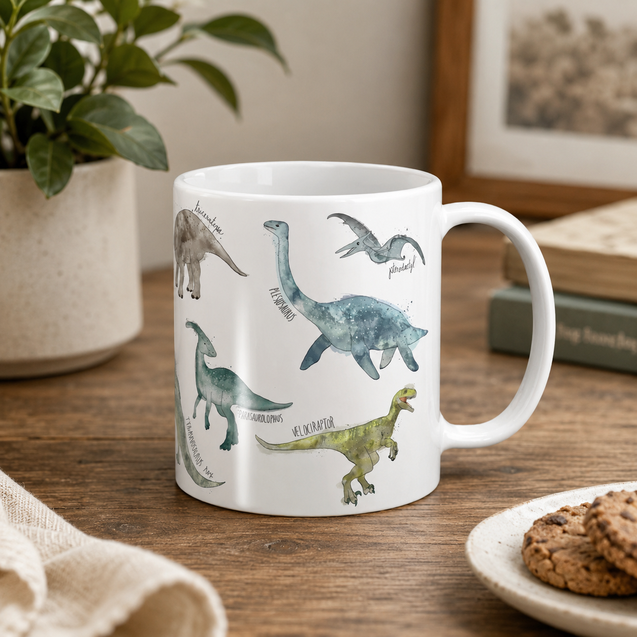 White mug with dinosaur illustrations on a wooden table with a plant and books in the background