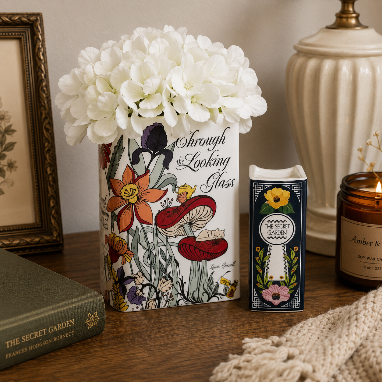 Decorative vase with floral design and text, candle, and book on a wooden surface.