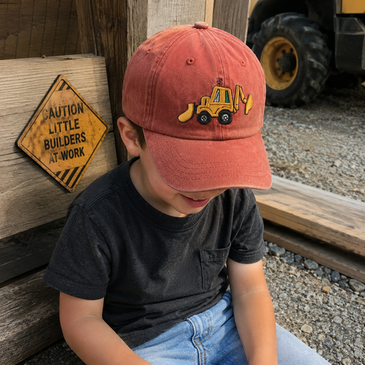 Child wearing a red cap with a bulldozer emblem, sitting next to a wooden block and warning sign.
