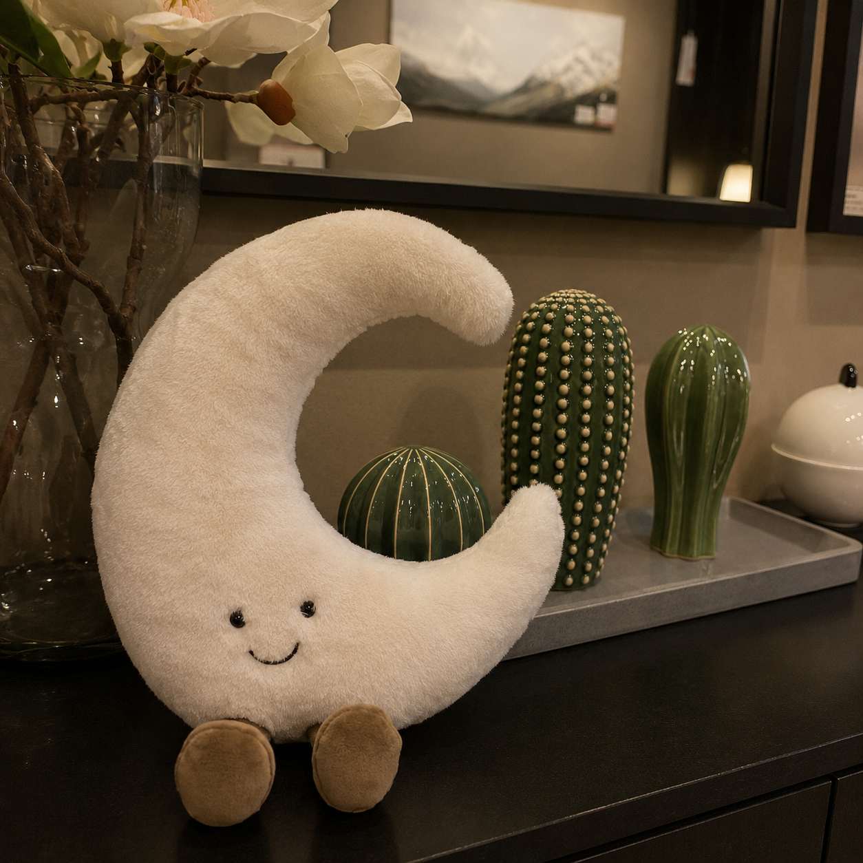 Plush moon toy on a table with decorative cacti and a vase in the background