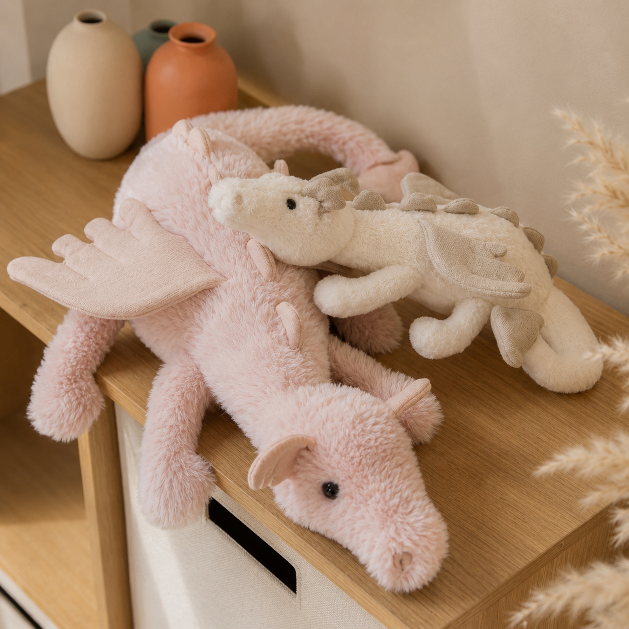 Two plush dragon toys on a wooden surface with decorative vases in the background.