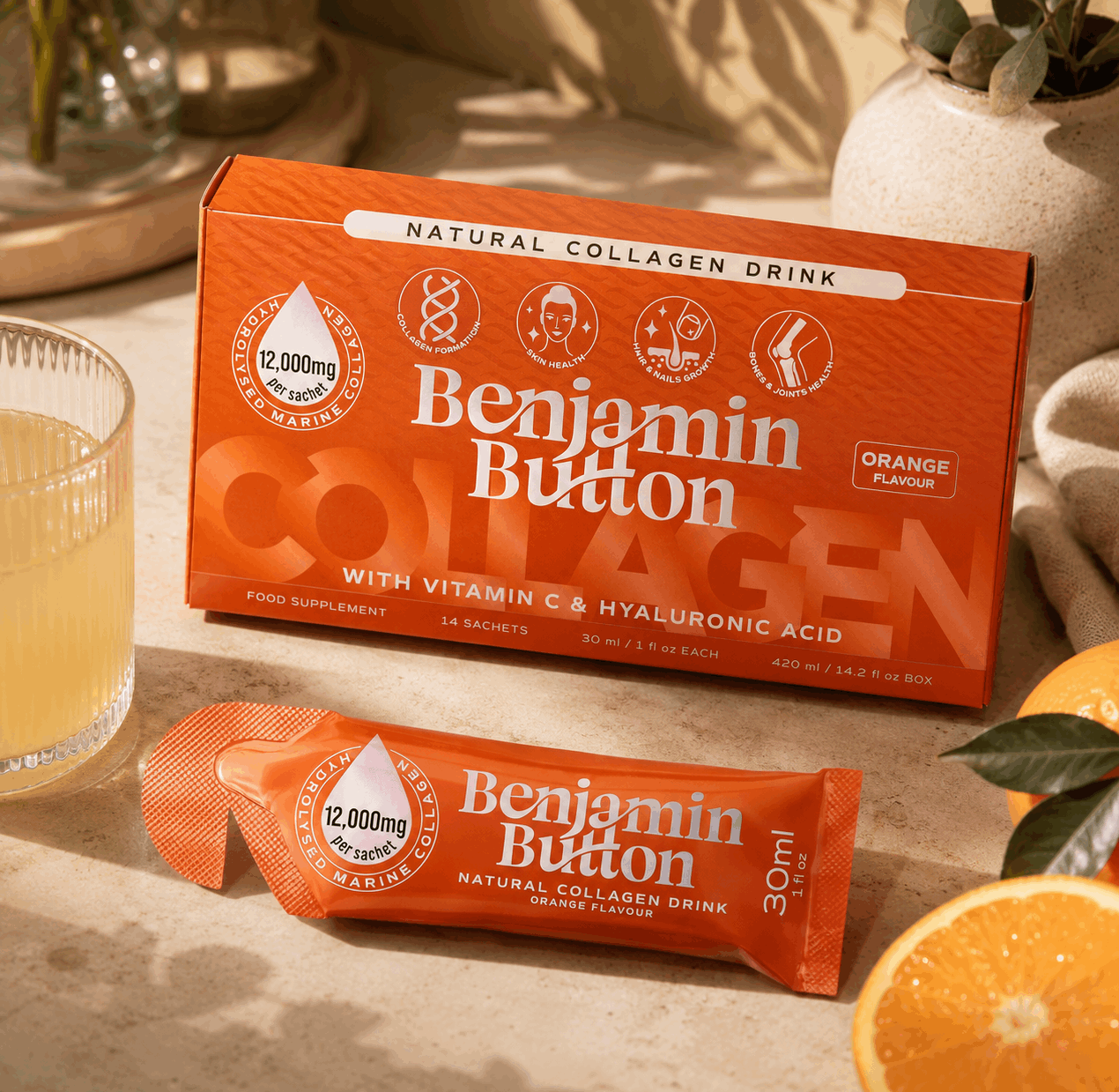 Benjamin Button Collagen drink packaging on a table with an orange and a glass of liquid.