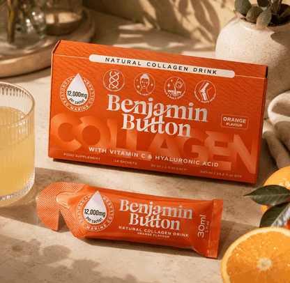 Benjamin Button Collagen drink packaging on a table with an orange and a glass of liquid.
