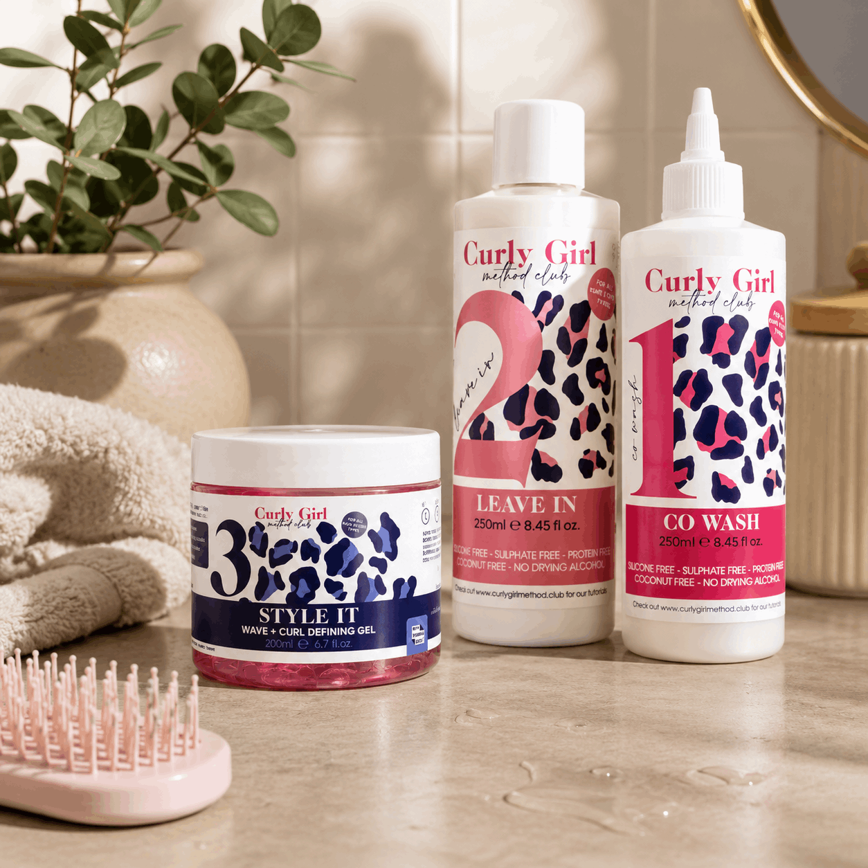 Curly Girl hair care products on a bathroom counter with a plant and towel in the background.