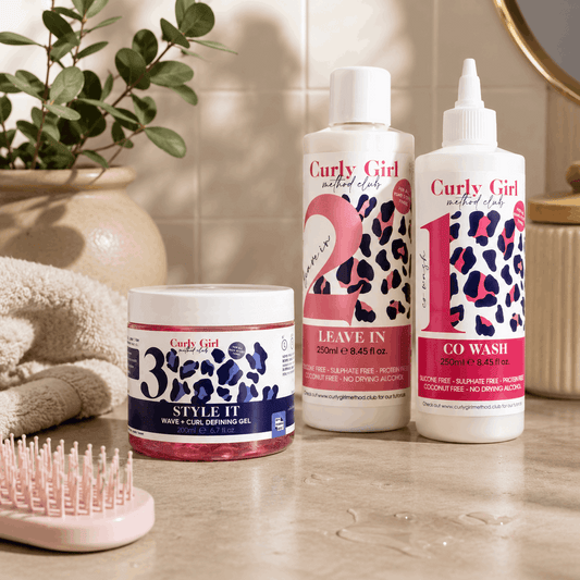 Curly Girl hair care products on a bathroom counter with a plant and towel in the background.