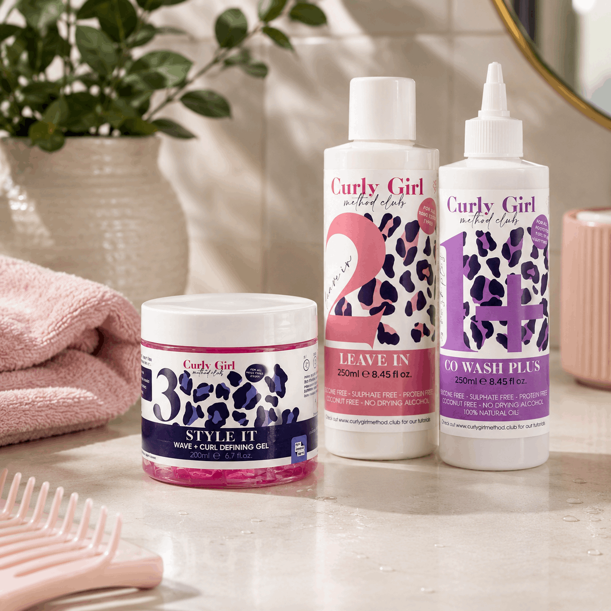 Curly Girl hair care products on a bathroom counter with a plant and towel in the background.