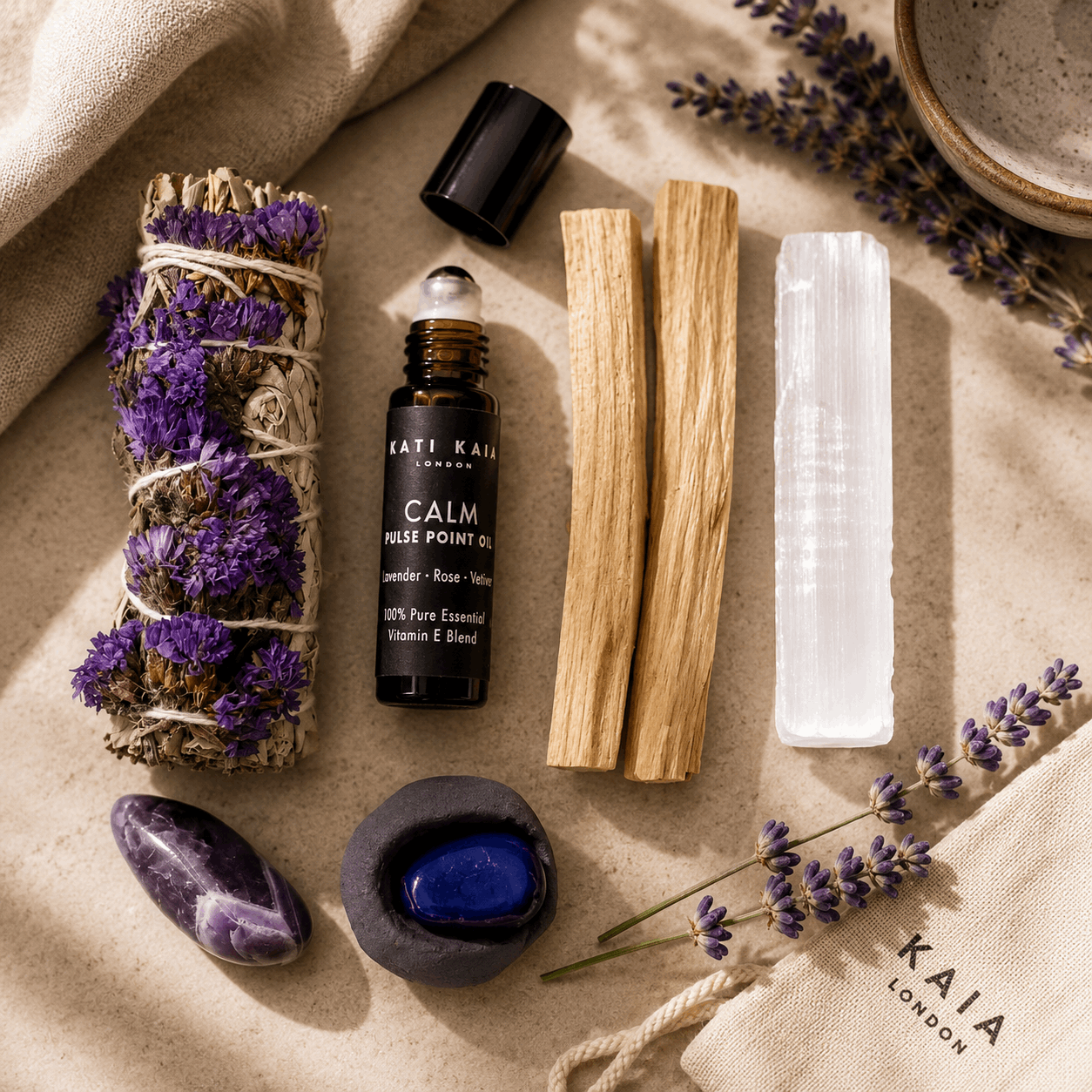 Collection of wellness items including a bottle of 'Calm' oil, lavender, and crystals on a textured surface.