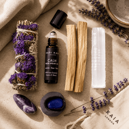 Collection of wellness items including a bottle of 'Calm' oil, lavender, and crystals on a textured surface.