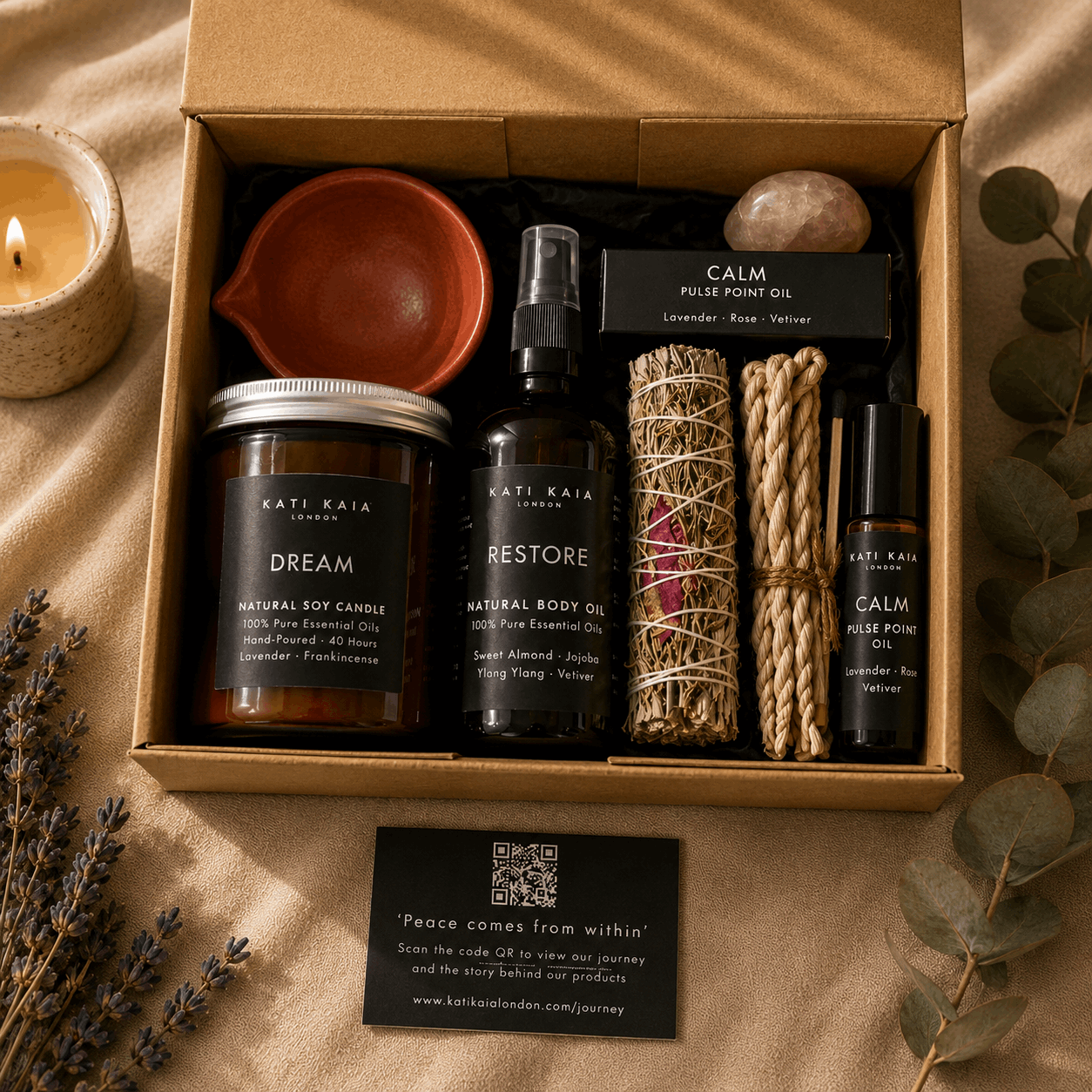 Box of Kati Kaia products including candles, oils, and a crystal on a beige background.