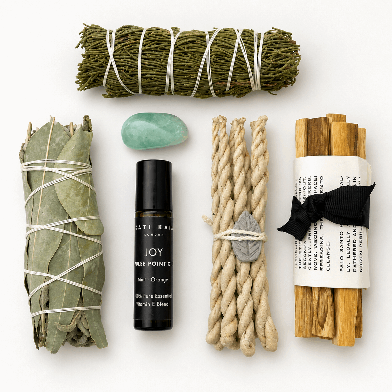 Collection of wellness items including sage, Palo Santo, and essential oil on a white background