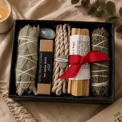 Gift set with smudge sticks, incense, and other items in a box on a textured surface.