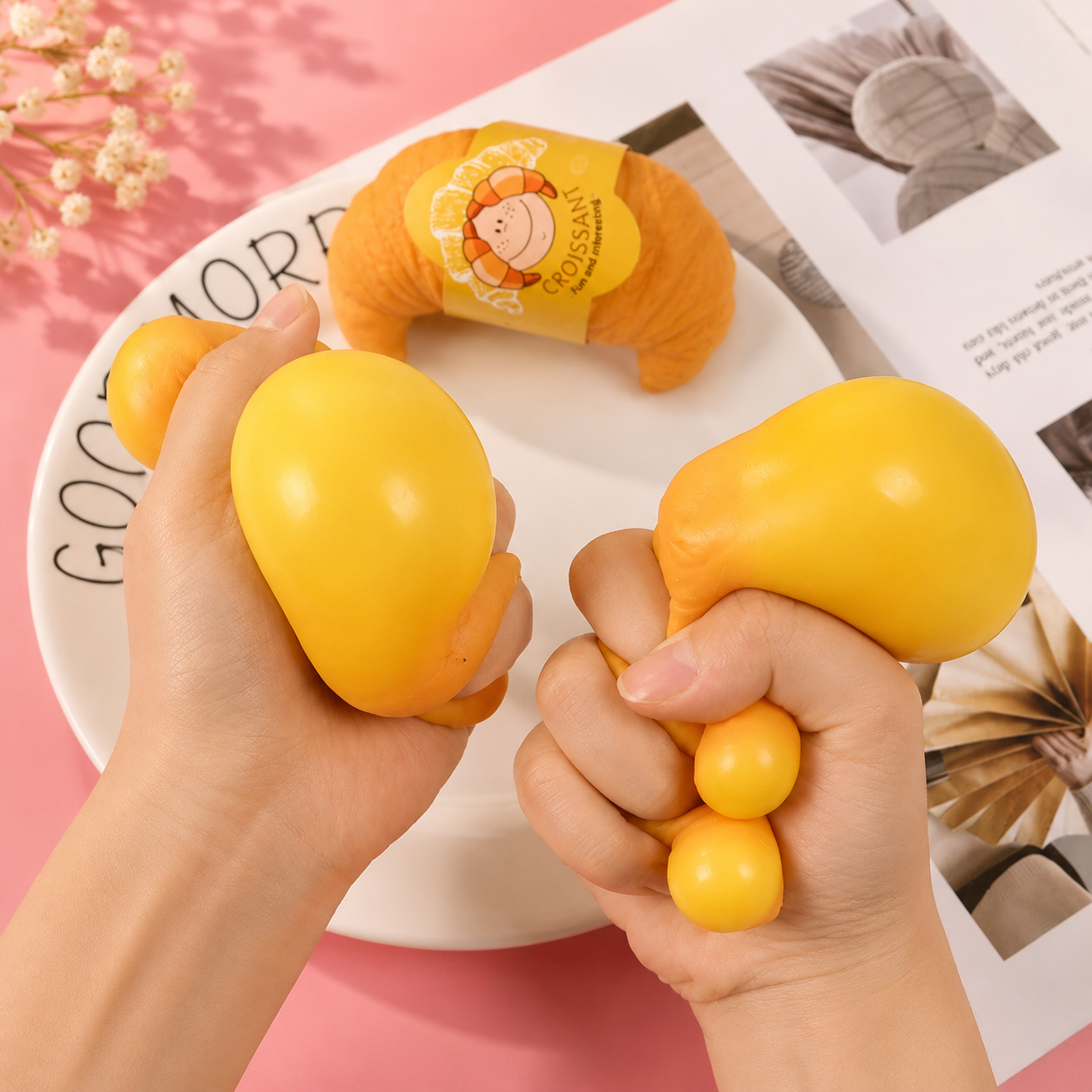 Yellow stress balls held by hands with a pink background and magazine.