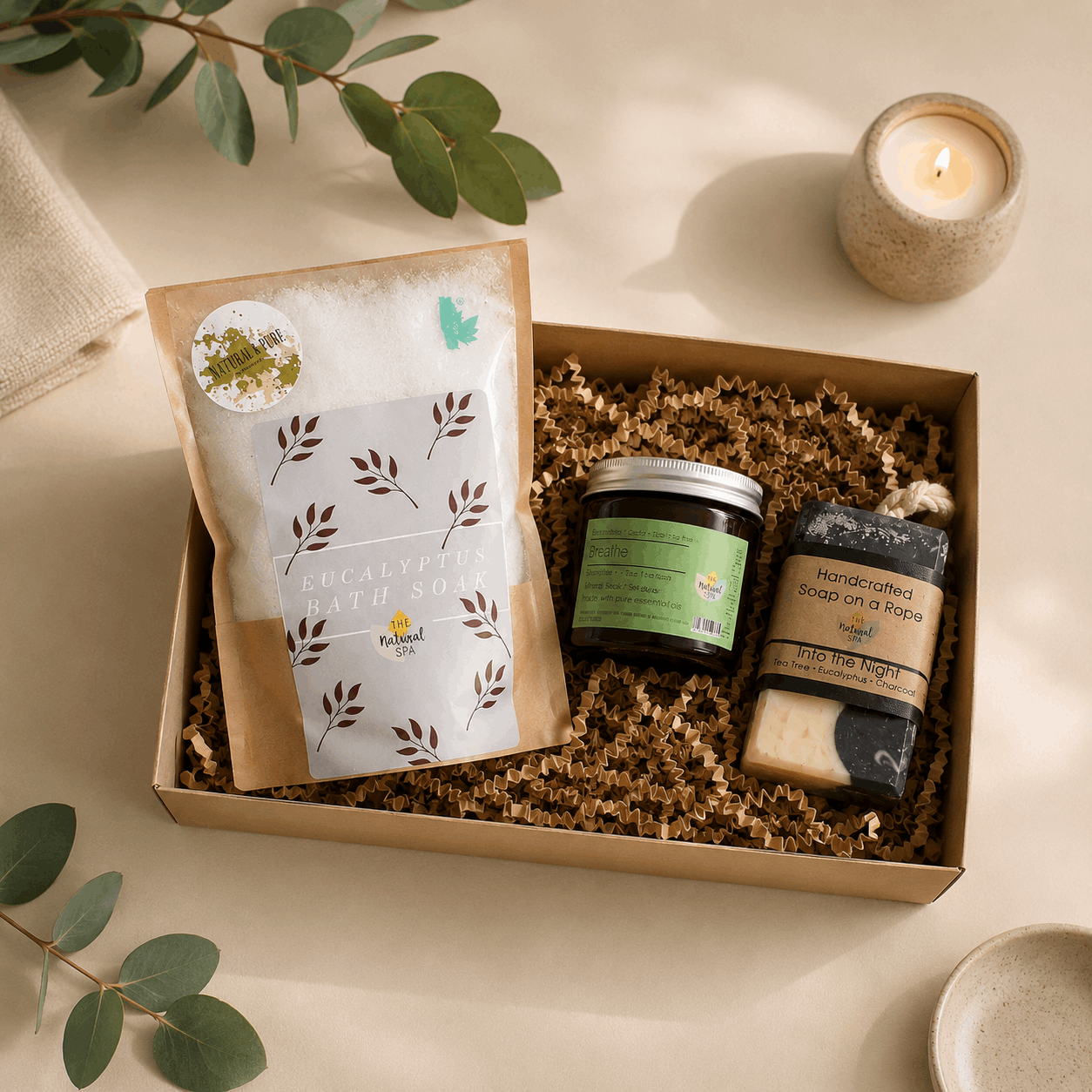 Gift box with natural products including soap, candle, and packaging on a light background