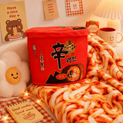 Red noodle bucket with Korean text on a bed with noodles and a notebook