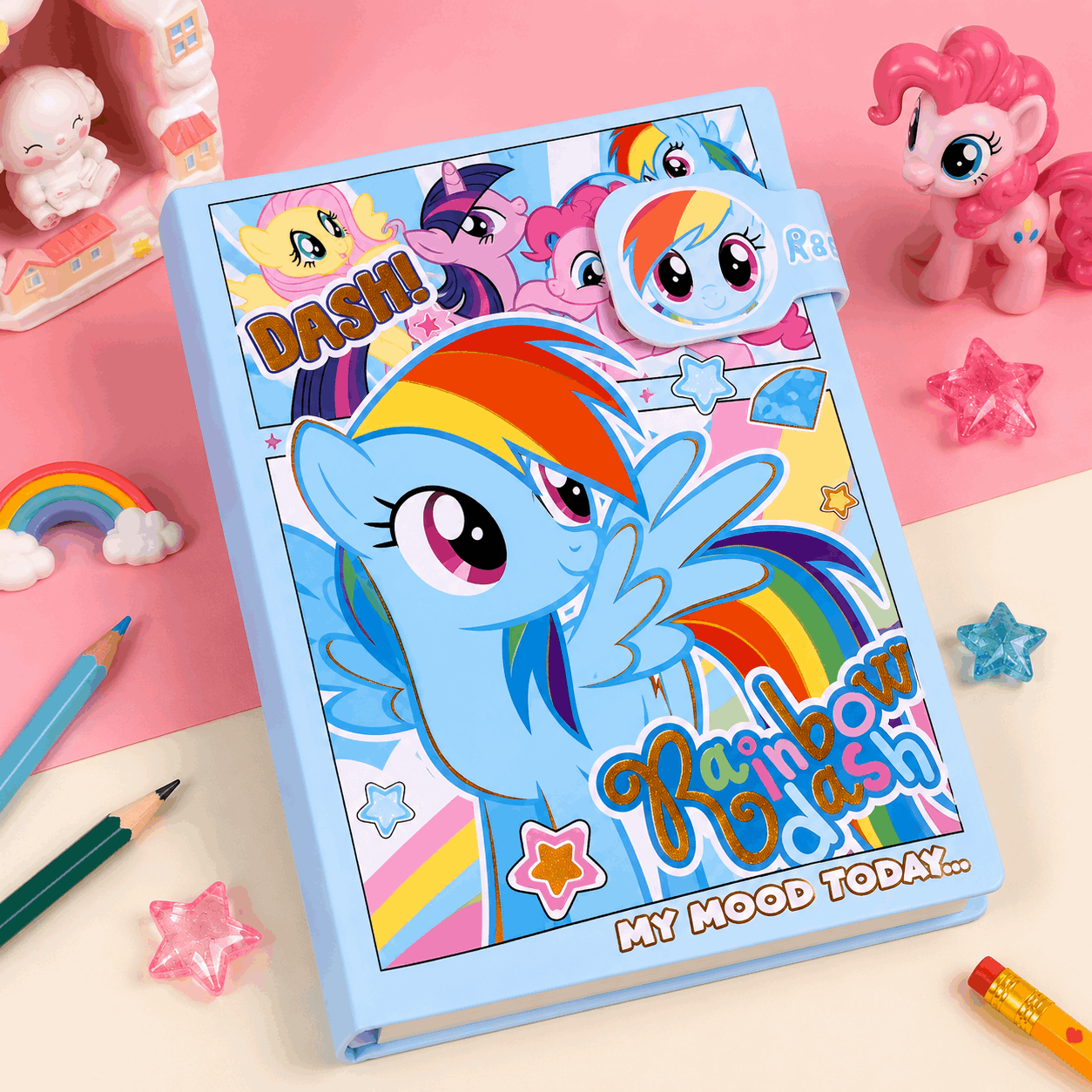 Notebook with Rainbow Dash design on a pink background with toys and stationery items.